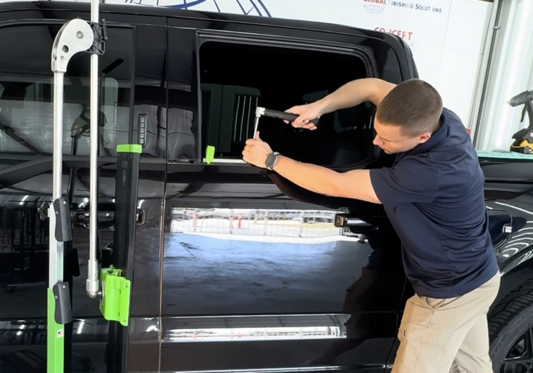 A technician uses specialized PDR tools to repair a dent on the aluminum door of a black Ford F-150 at our Houston shop.