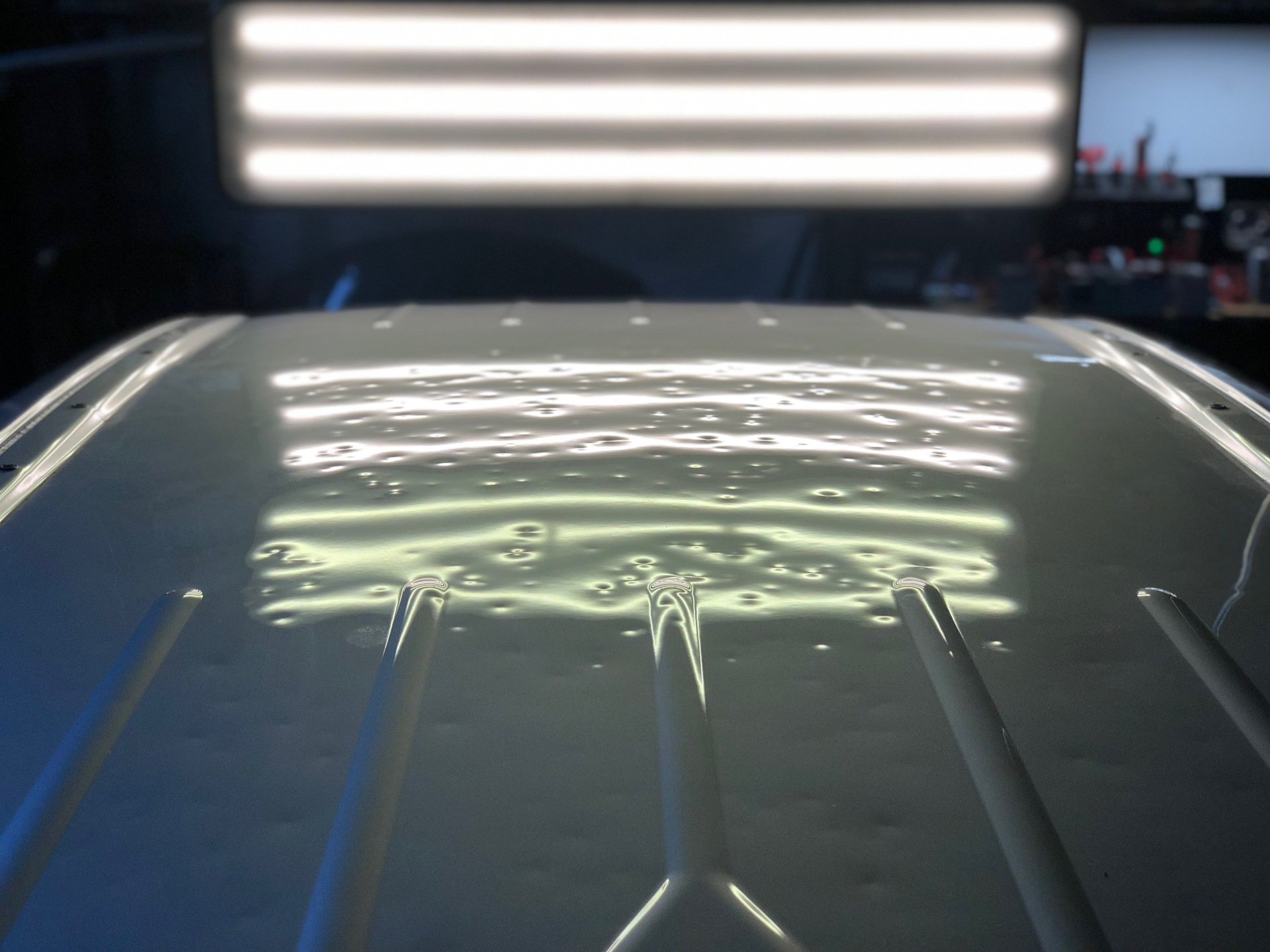 Car roof covered in hail dents, shown under LED light-board reflections