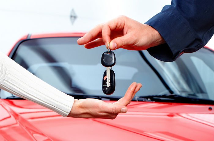 Car keys being handed over in front of a red car